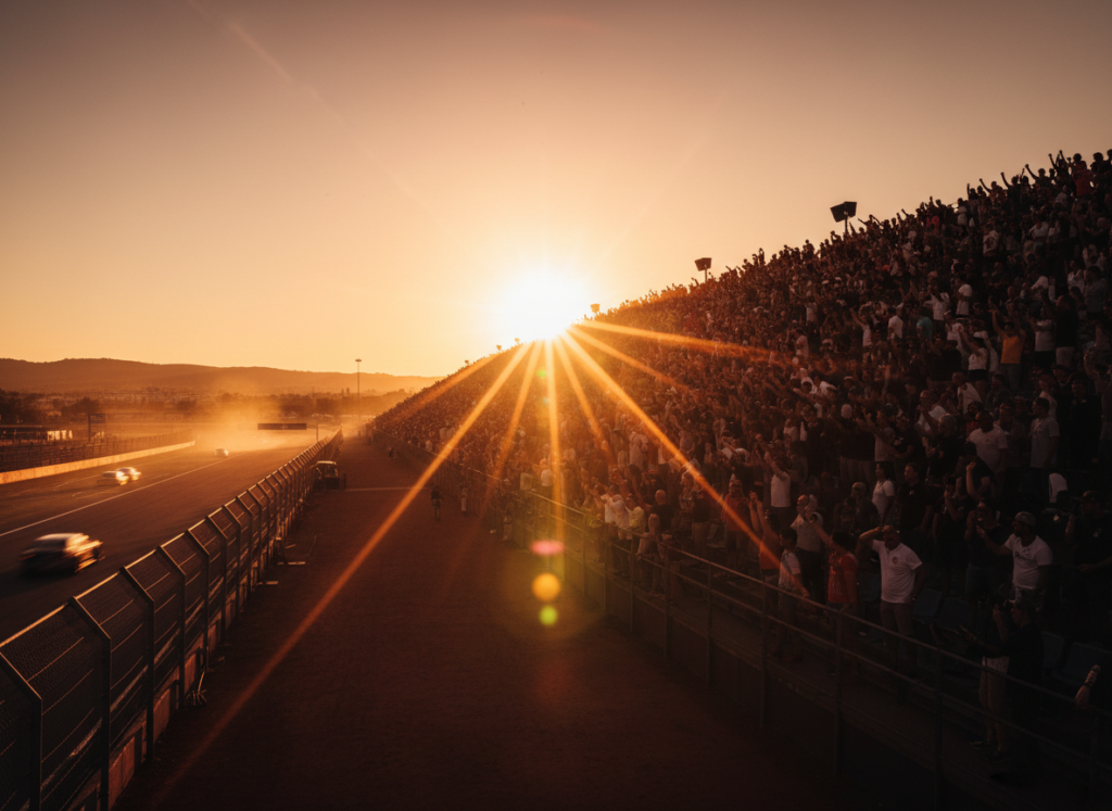 Packed grandstand at a racetrack during golden hour